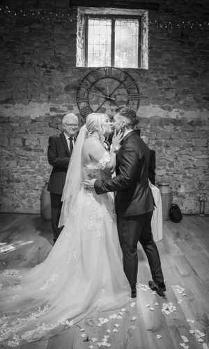 Black and white first look photos of couple dancing in rustic stone venue with scattered rose petals.