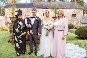 A group of wedding guests pose together on a lawn in front of a rustic stone building.