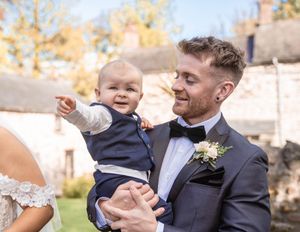 Wedding party members interacting with a small child during outdoor autumn celebrations.