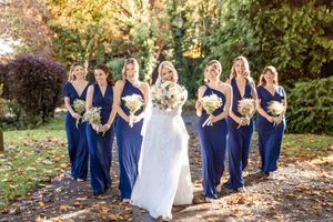 Bridal party poses for photos in a line outside during autumn with colorful fall foliage in the background.
