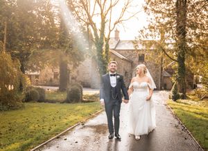 A newlywed couple walks down a misty garden path surrounded by trees on their wedding day.