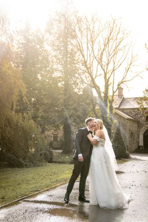 Newlyweds share romantic moment in misty garden path during golden hour.