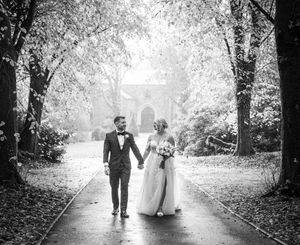 Black and white photo of couple walking down tree-lined path on wedding day.