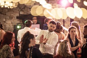 Wedding guests dancing and celebrating at a reception under warm glowing lights in a rustic stone venue.