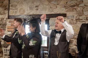 A group of people dancing and celebrating against exposed stone walls at an indoor wedding venue.