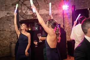 Guests dancing and celebrating at a dimly lit wedding reception with brick walls and string lights.