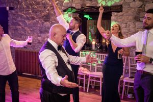 Wedding guests dancing and celebrating on a dance floor inside a historic stone building with pink lighting.