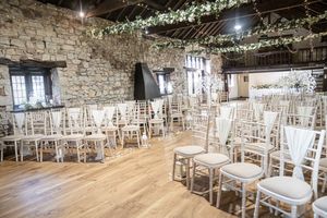 Rustic stone wall venue decorated with white floral garlands and elegant chiavari chairs set up for a wedding ceremony.