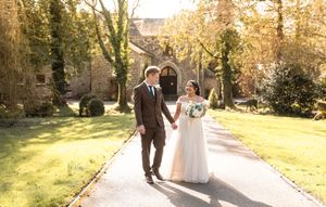A couple walks along a sunlit garden path during a romantic outdoor photo session at golden hour.