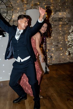 Energetic couple dancing at a wedding reception with twinkle lights and rustic decor in the background.
