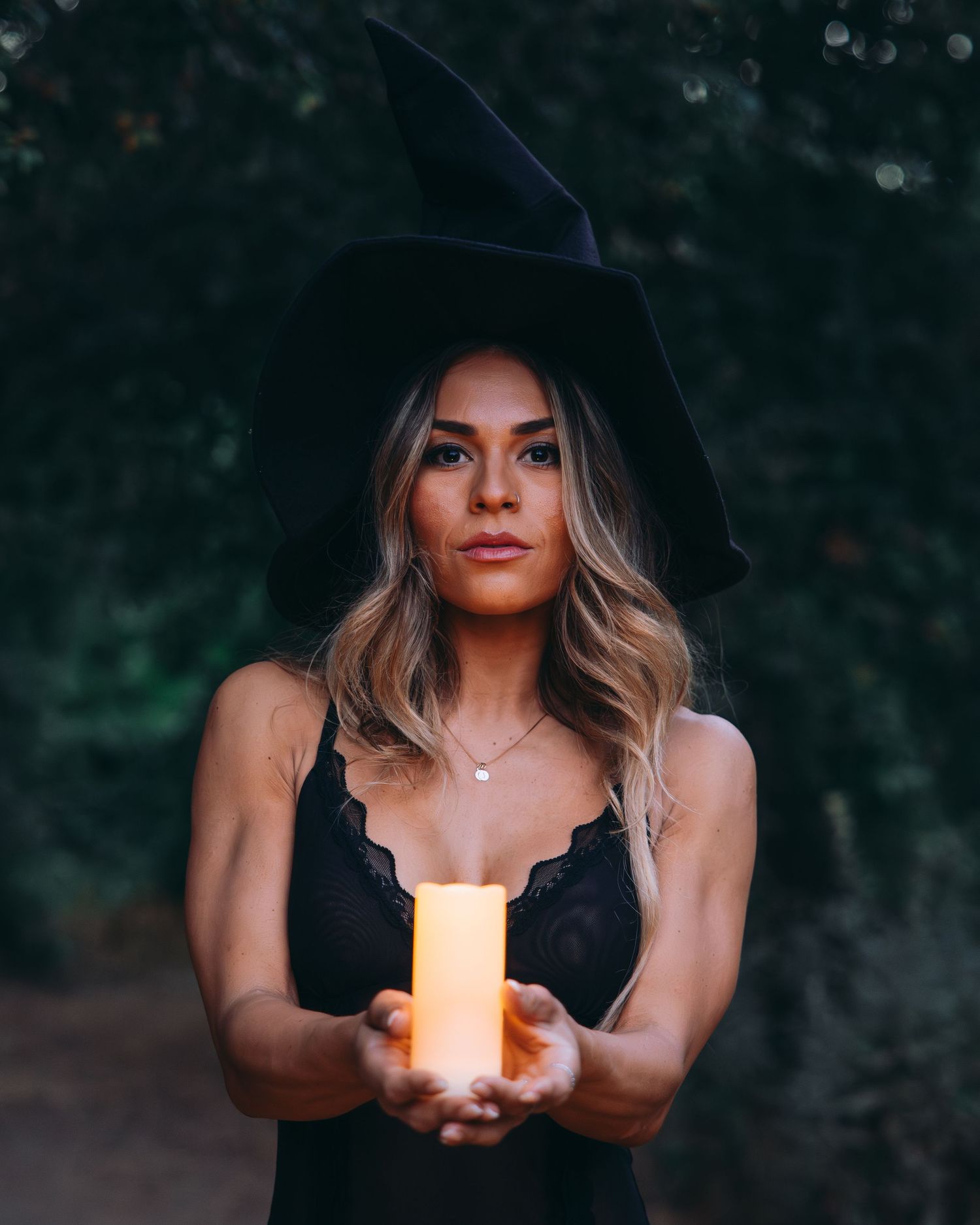 Atmospheric outdoor photography with glowing candles casting warm light against dark forest background.