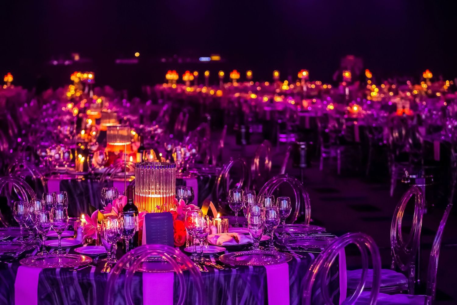 Elegant wedding reception hall decorated with purple uplighting and crystal chandeliers on dining tables.