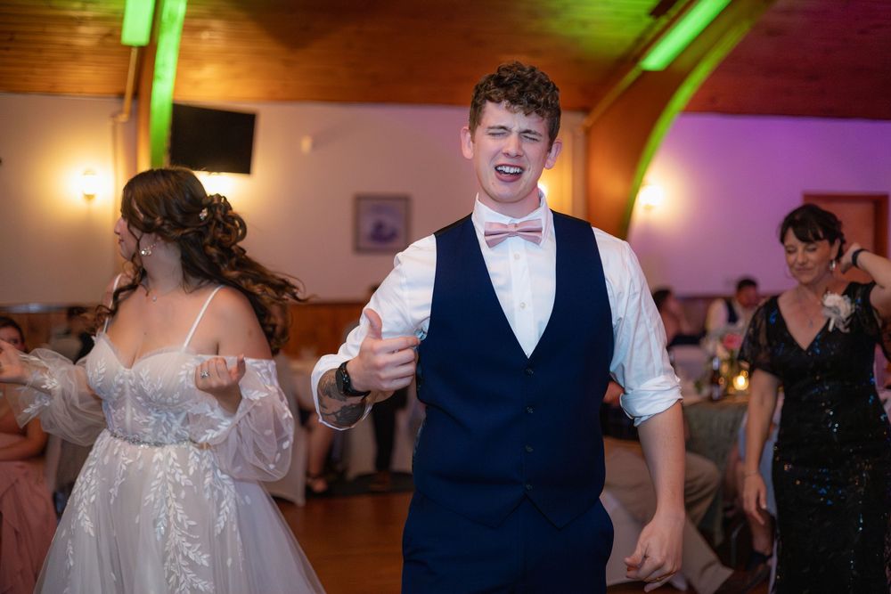 Wedding guests enjoy dancing on a colorfully lit dance floor with green lighting and decorations at a reception celebration.