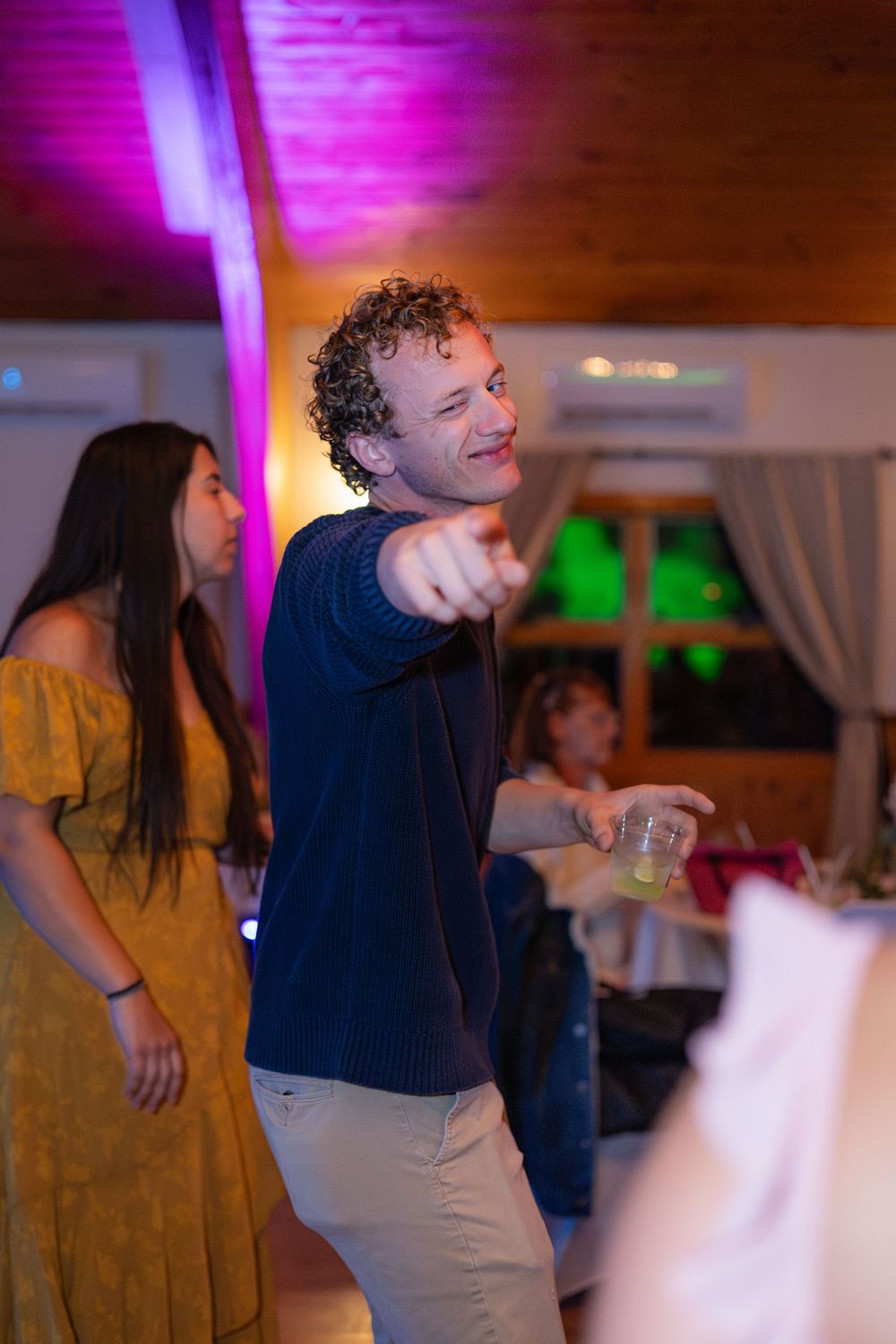 Wedding guests dance and celebrate on a dimly lit dance floor with purple and pink lighting effects.