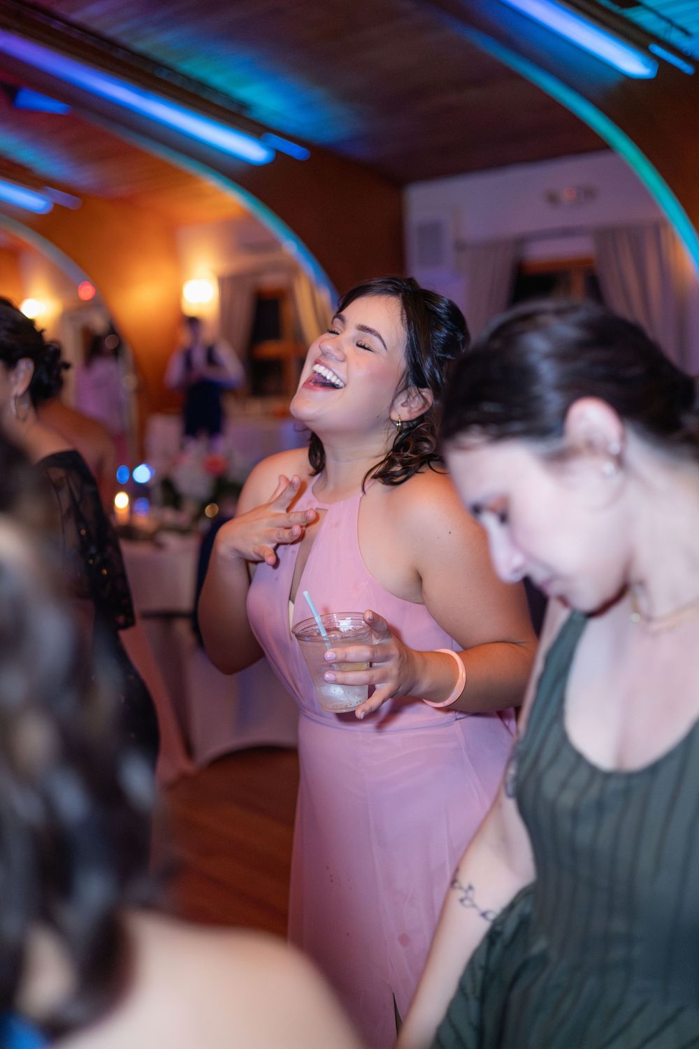 A guest in a pink dress dancing joyfully at a wedding reception with blue lighting overhead.
