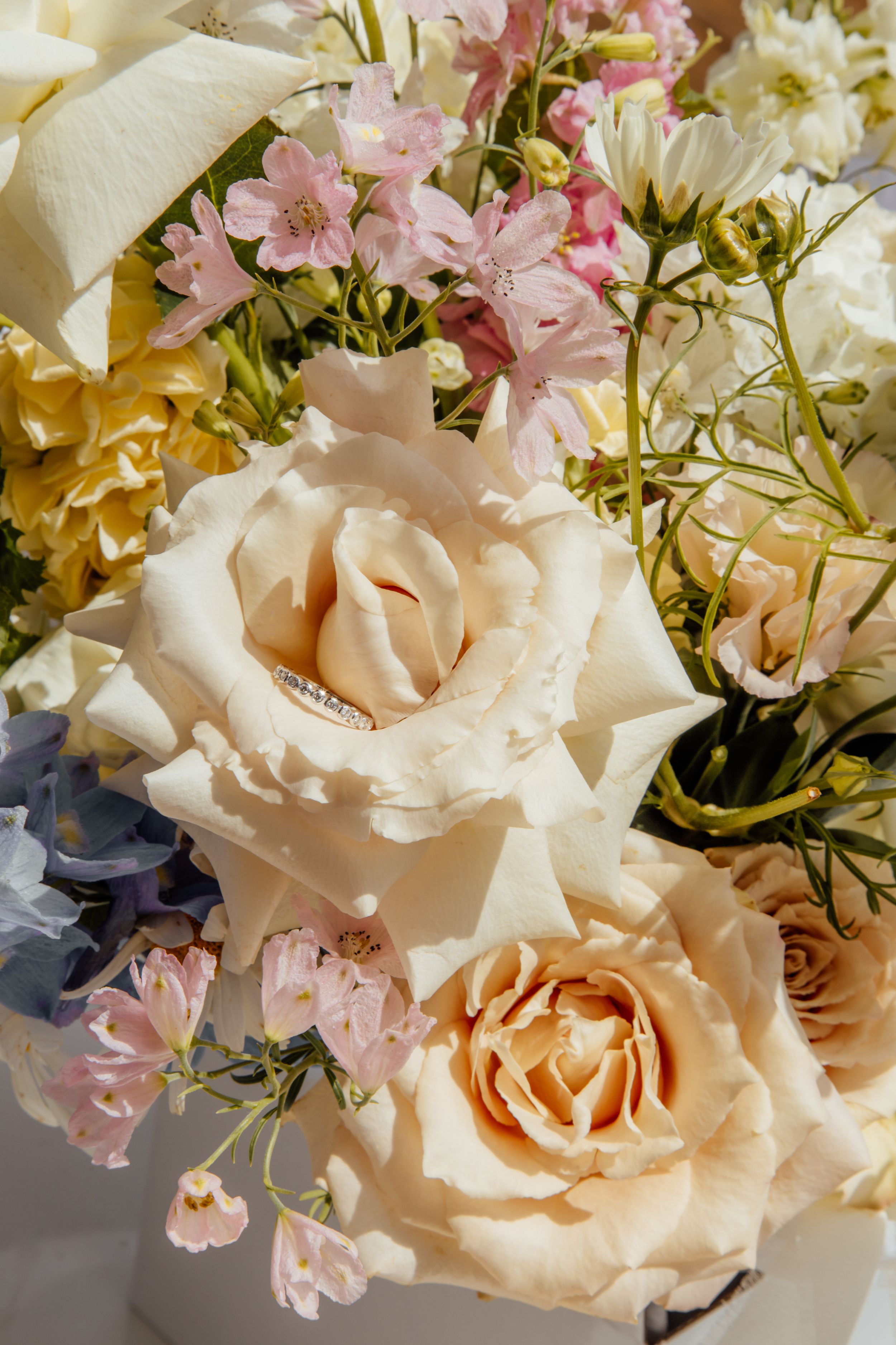 Close-up of pale peach roses and pink delicate flowers in a romantic floral arrangement with soft natural lighting.