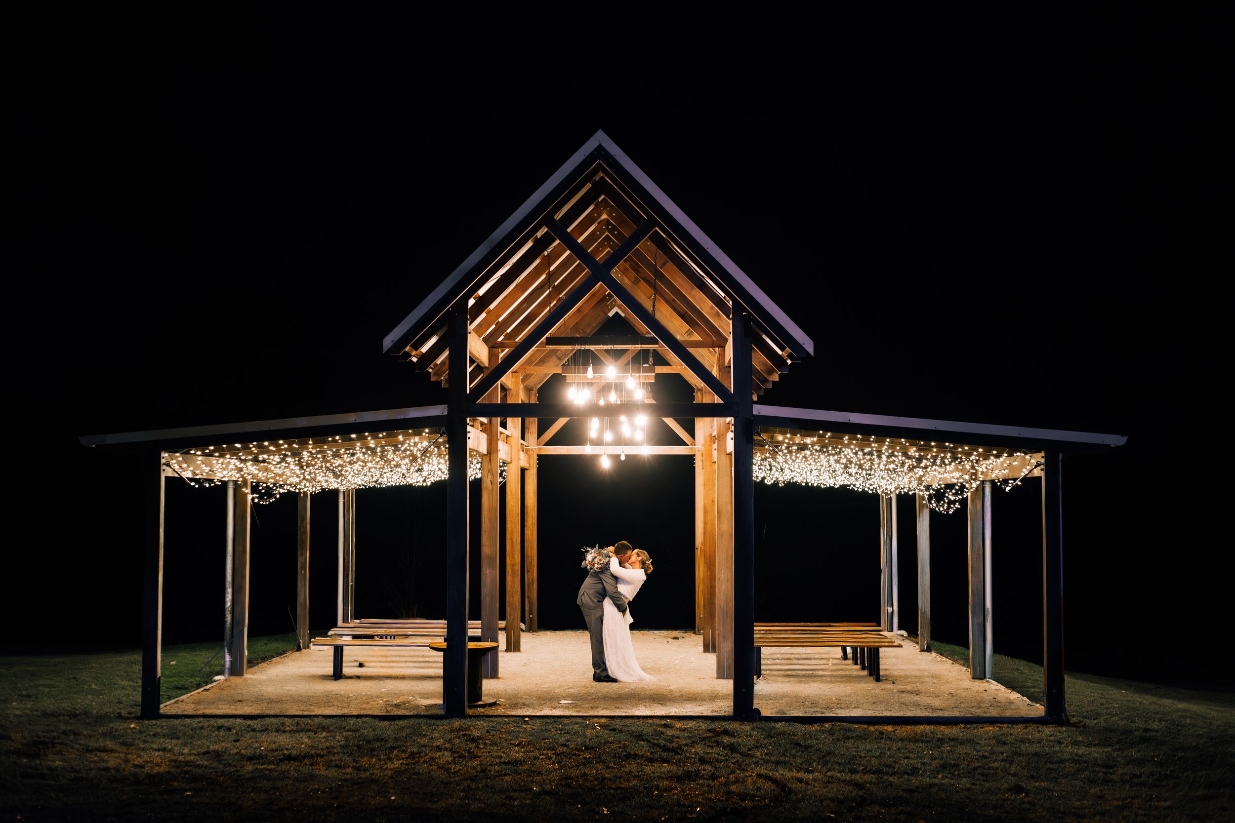 String lights illuminate an outdoor covered pavilion at night during a romantic event celebration.
