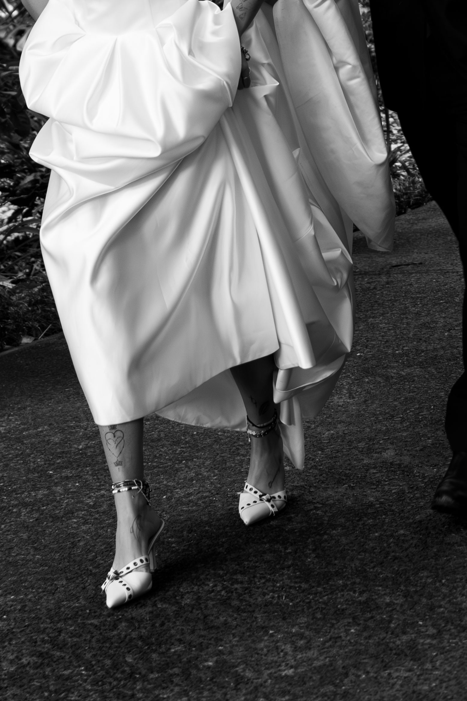 Low angle shot of white wedding dress and jeweled bridal shoes on dark ground in black and white photography.