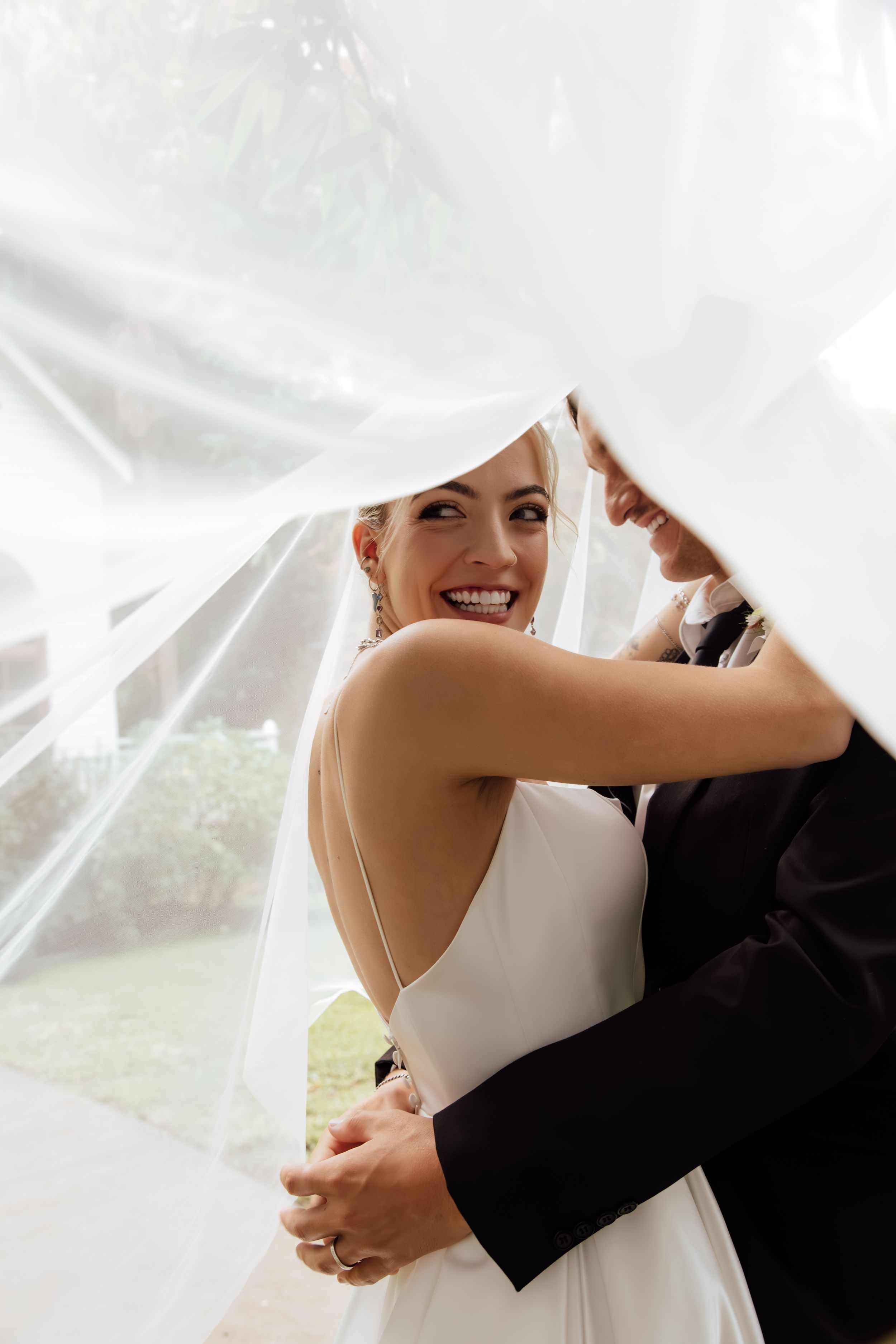 Four sequential wedding photos show a couple in black and white attire embracing under a white tent.