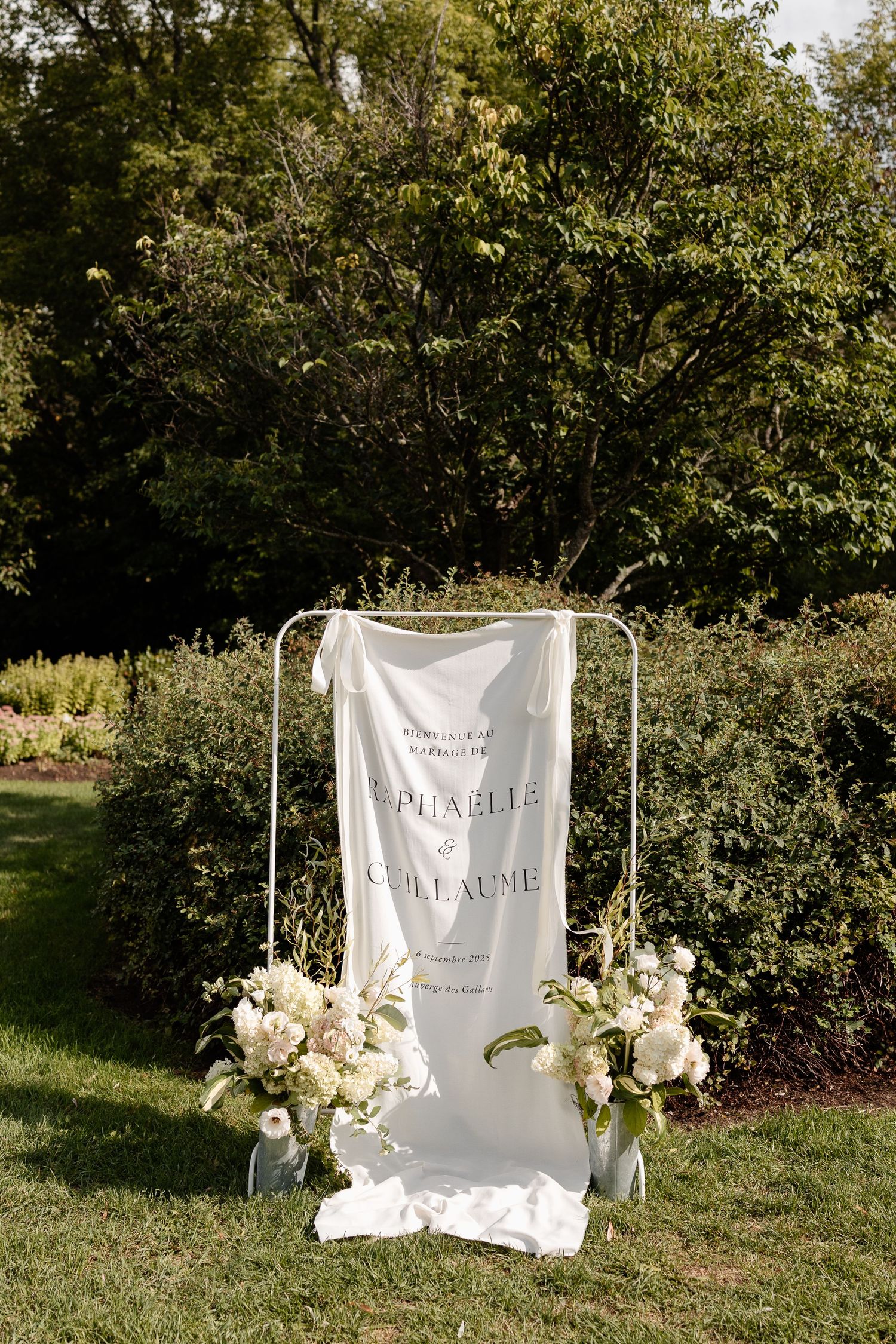 White fabric backdrop with floral decorations and 'Palladine' text displayed in an outdoor garden setting.