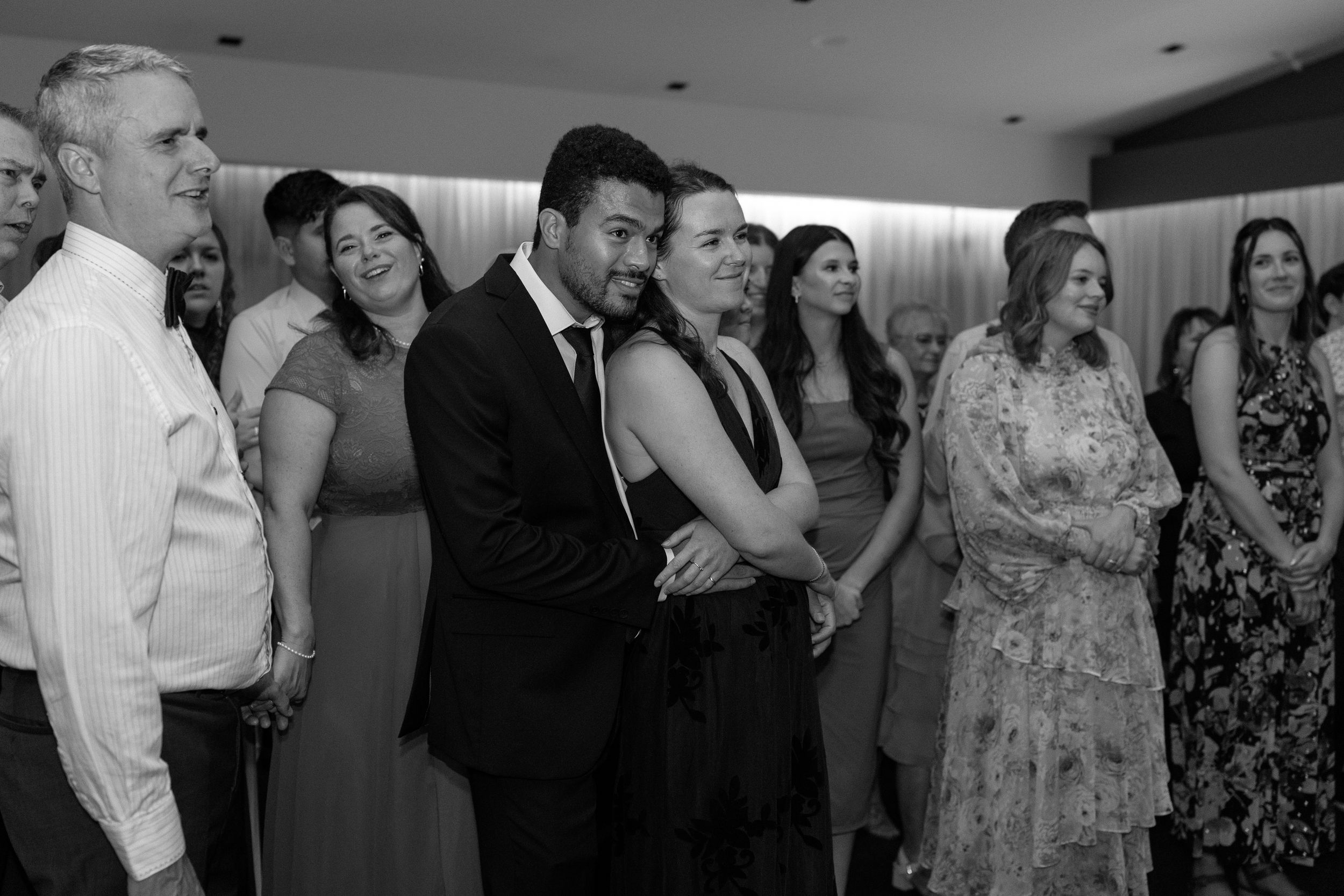 A black and white photo of guests mingling and conversing at an elegant indoor reception event.
