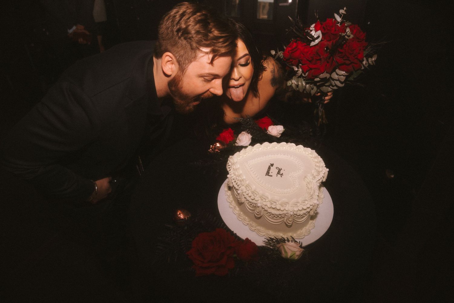 Romantic couple enjoys intimate moment during sunset wedding ceremony with red floral decorations.