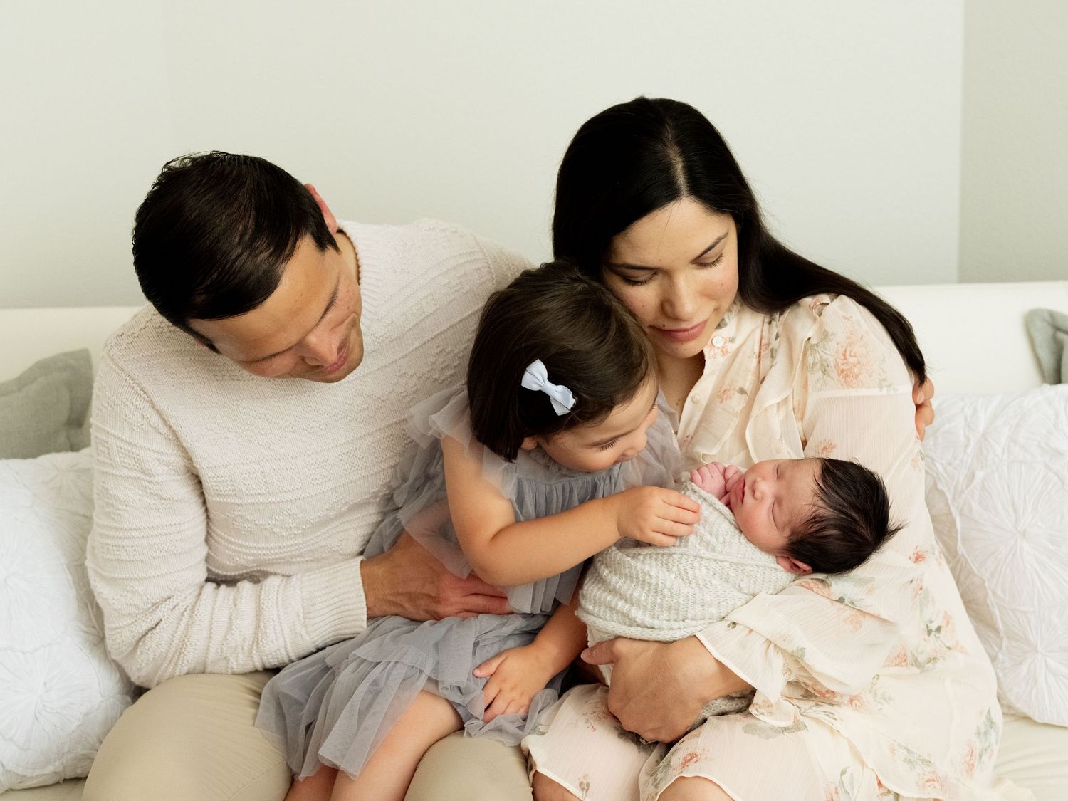 Four tender moments showing parents bonding with their newborn baby on a bed with white linens.