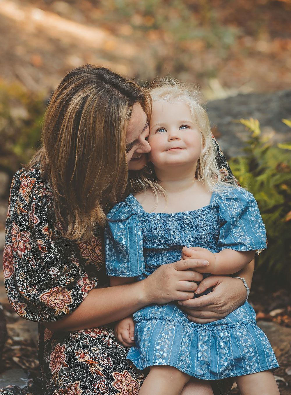 A tender moment captured in nature showing a close embrace between two people wearing blue and floral patterned dresses.