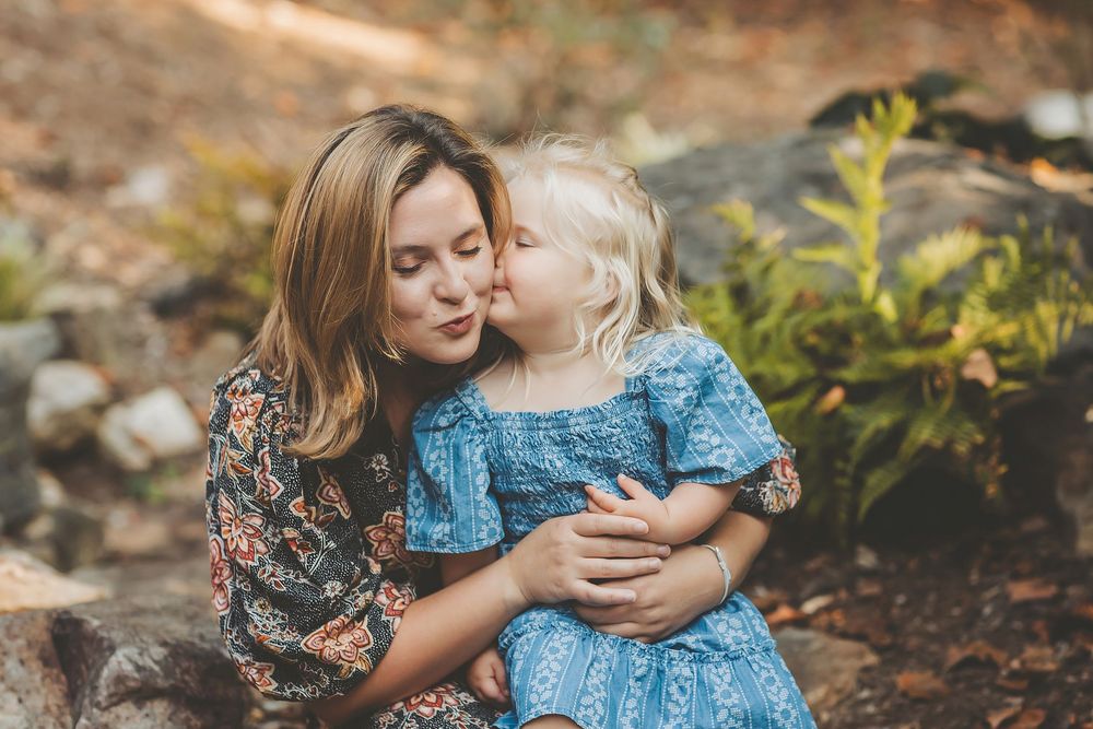 Mother and daughter share tender embraces in a scenic outdoor setting wearing coordinated blue dresses.
