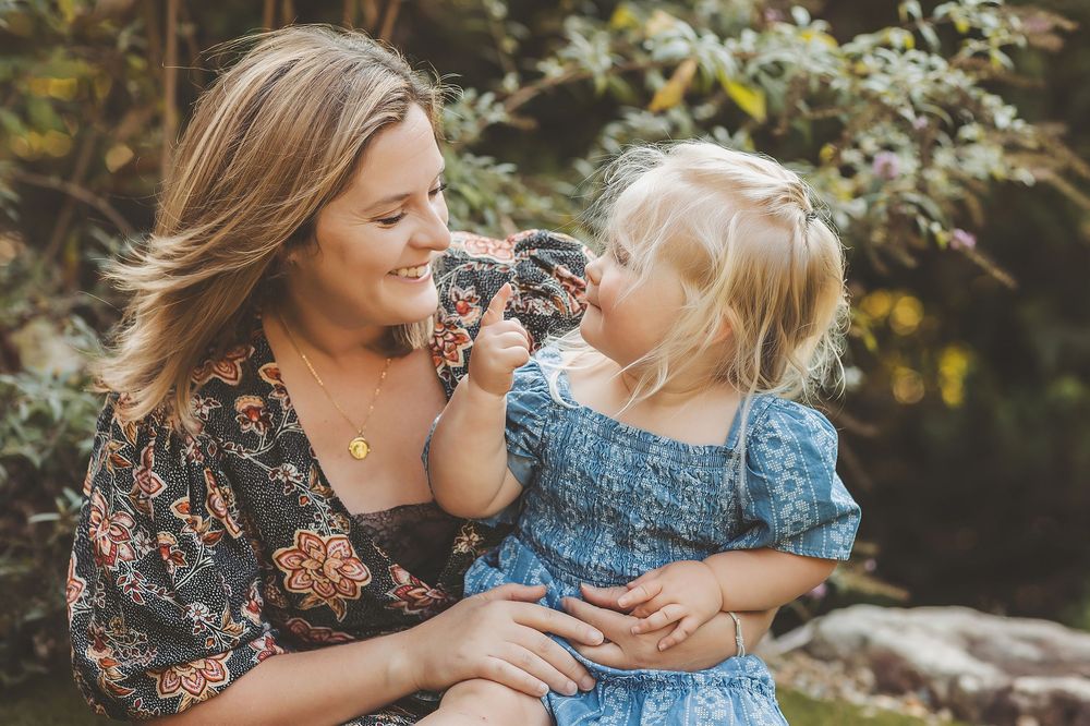 A mother and child share joyful moments together in a lush outdoor garden setting during a photo session.