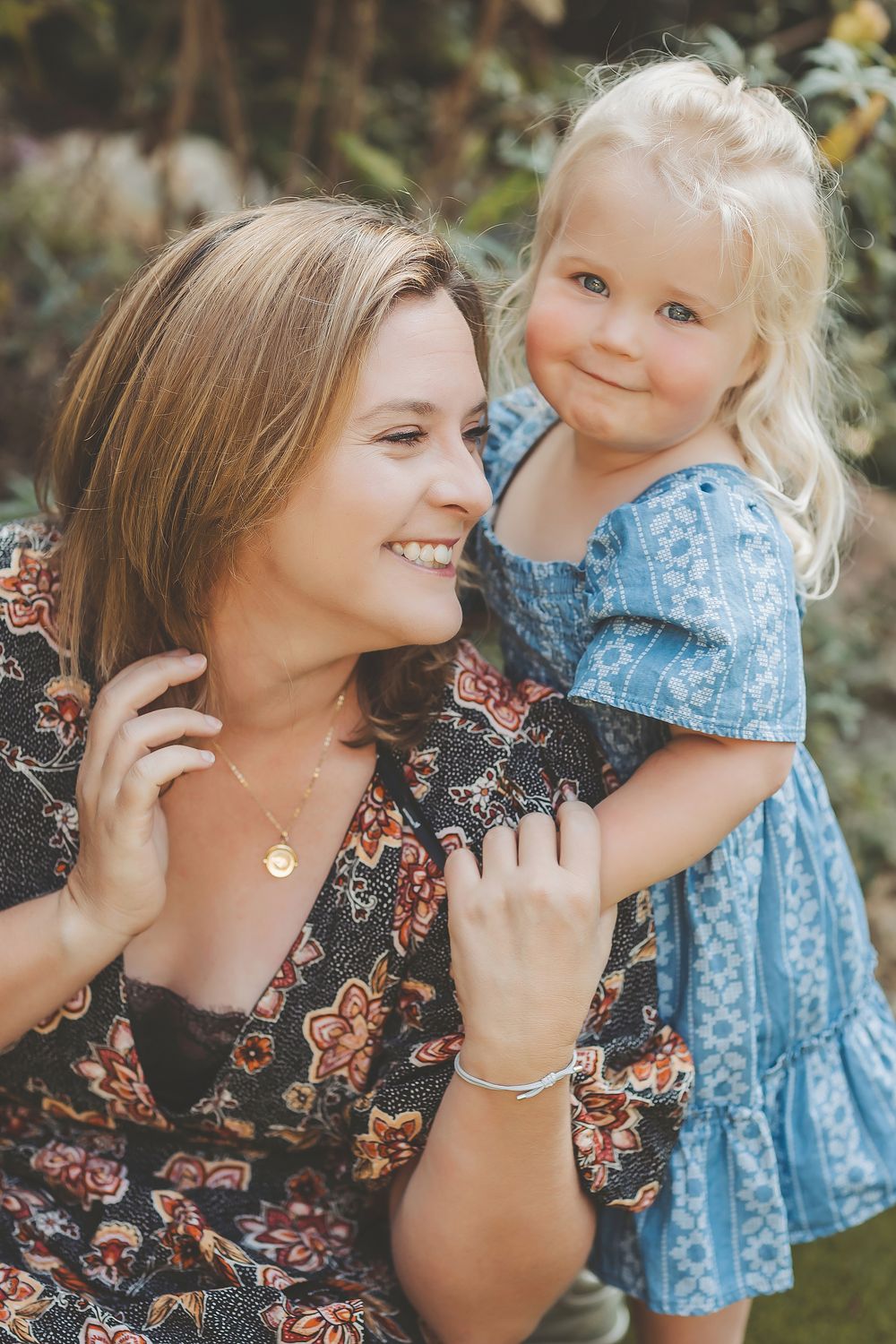 A tender moment captured in a garden setting showing affectionate interaction while wearing floral and blue patterned dresses.