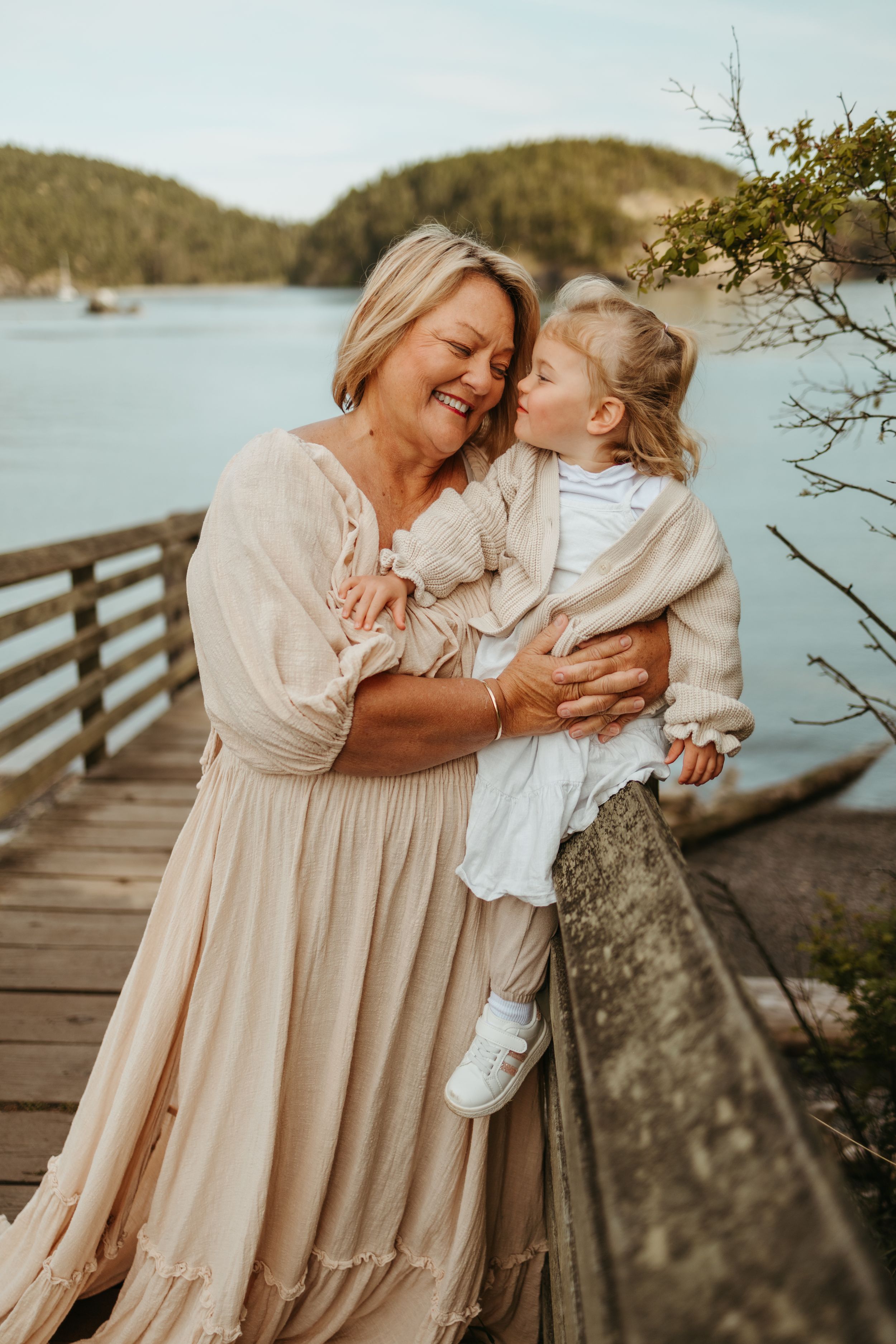 Mother and daughter share tender moments on a wooden dock by the water during a sunset photoshoot.