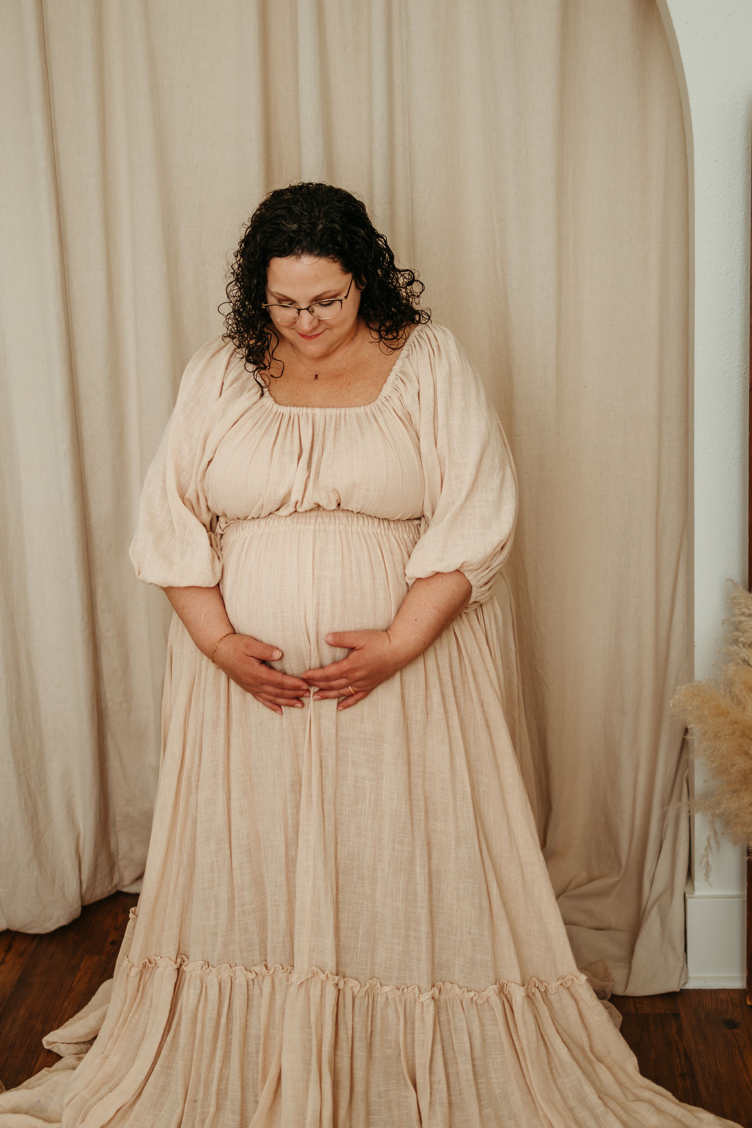 Woman wearing a flowy cream-colored prairie dress with puff sleeves stands against a beige curtain backdrop.