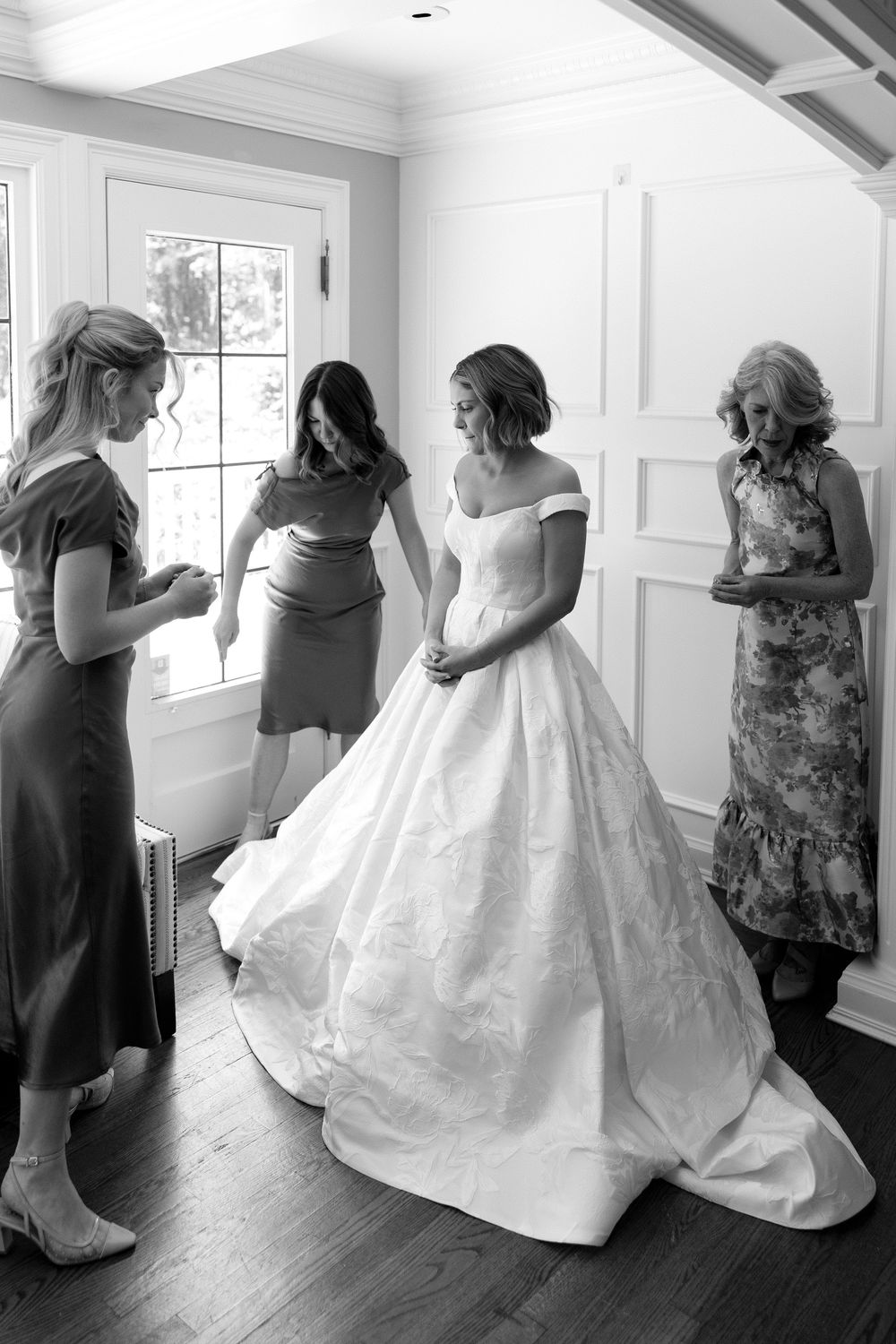 A sequence of black and white photos showing a bride getting dressed in a flowing white wedding gown.