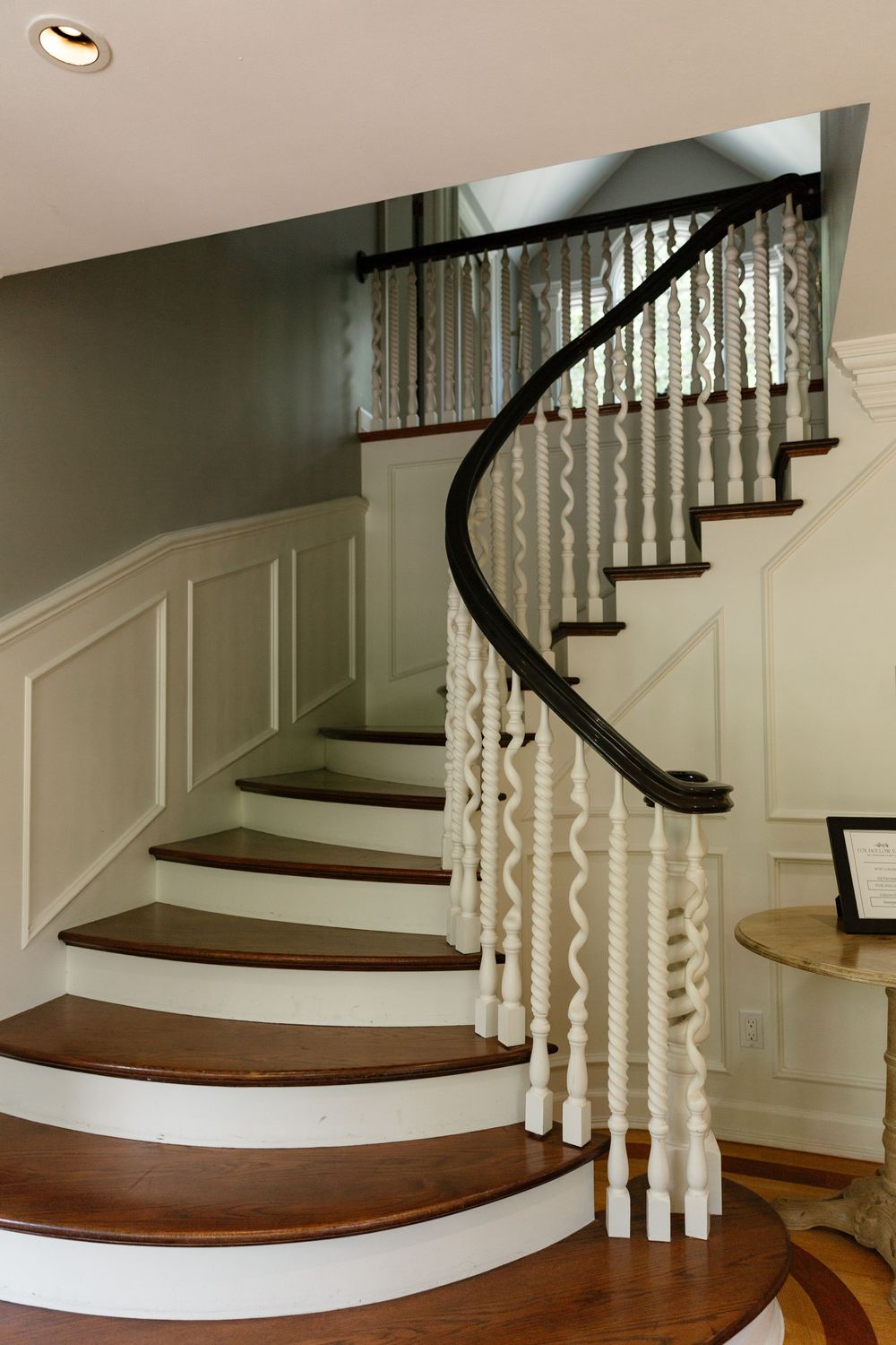 Elegant curved staircase with dark wood treads, white risers, and ornate white spindles against sage green walls.