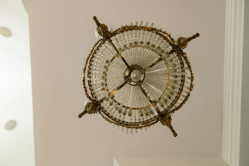 Three ornate crystal chandeliers hang from a white ceiling in an elegant room.