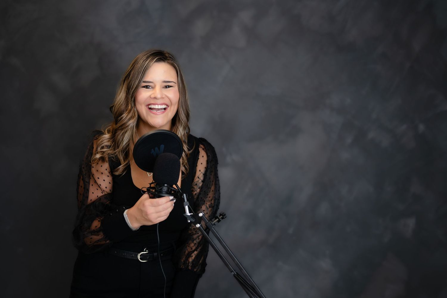 Professional photographer in black lace holding camera against dark backdrop.