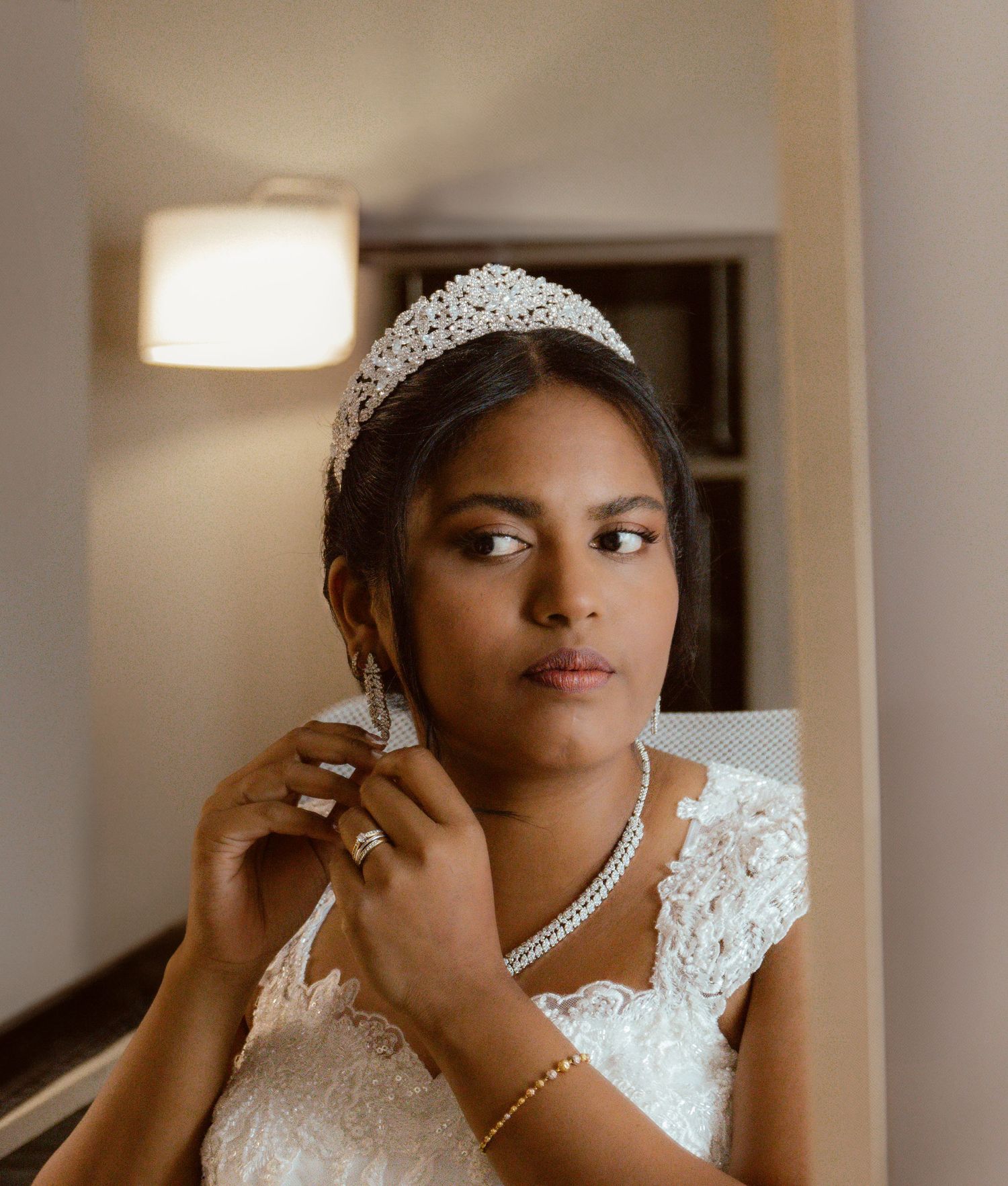 An elegant bride wearing a sparkling tiara and necklace in soft lighting.