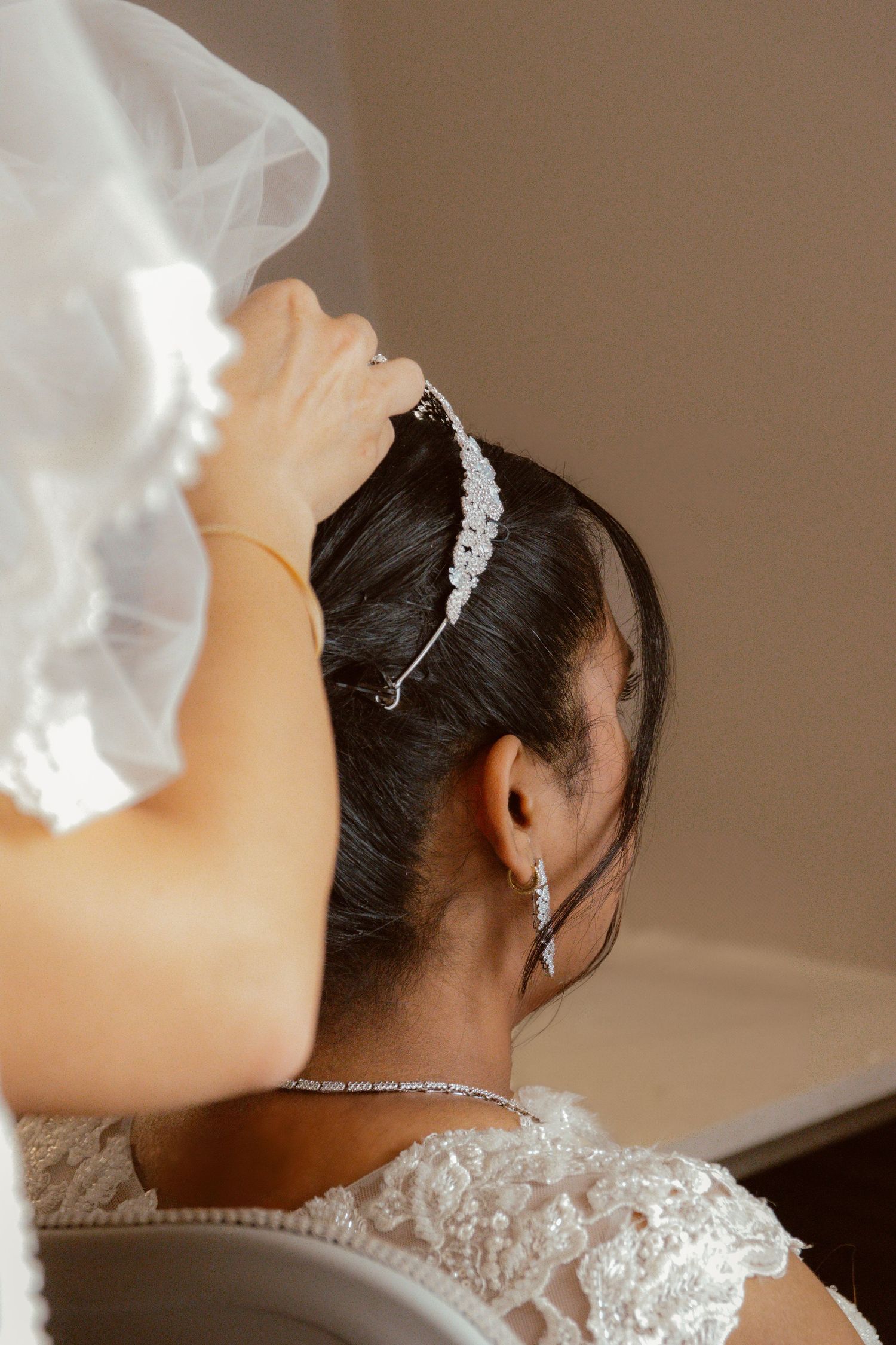 Back view of a bride wearing lace wedding dress and crystal hair accessory with veil on her wedding day.
