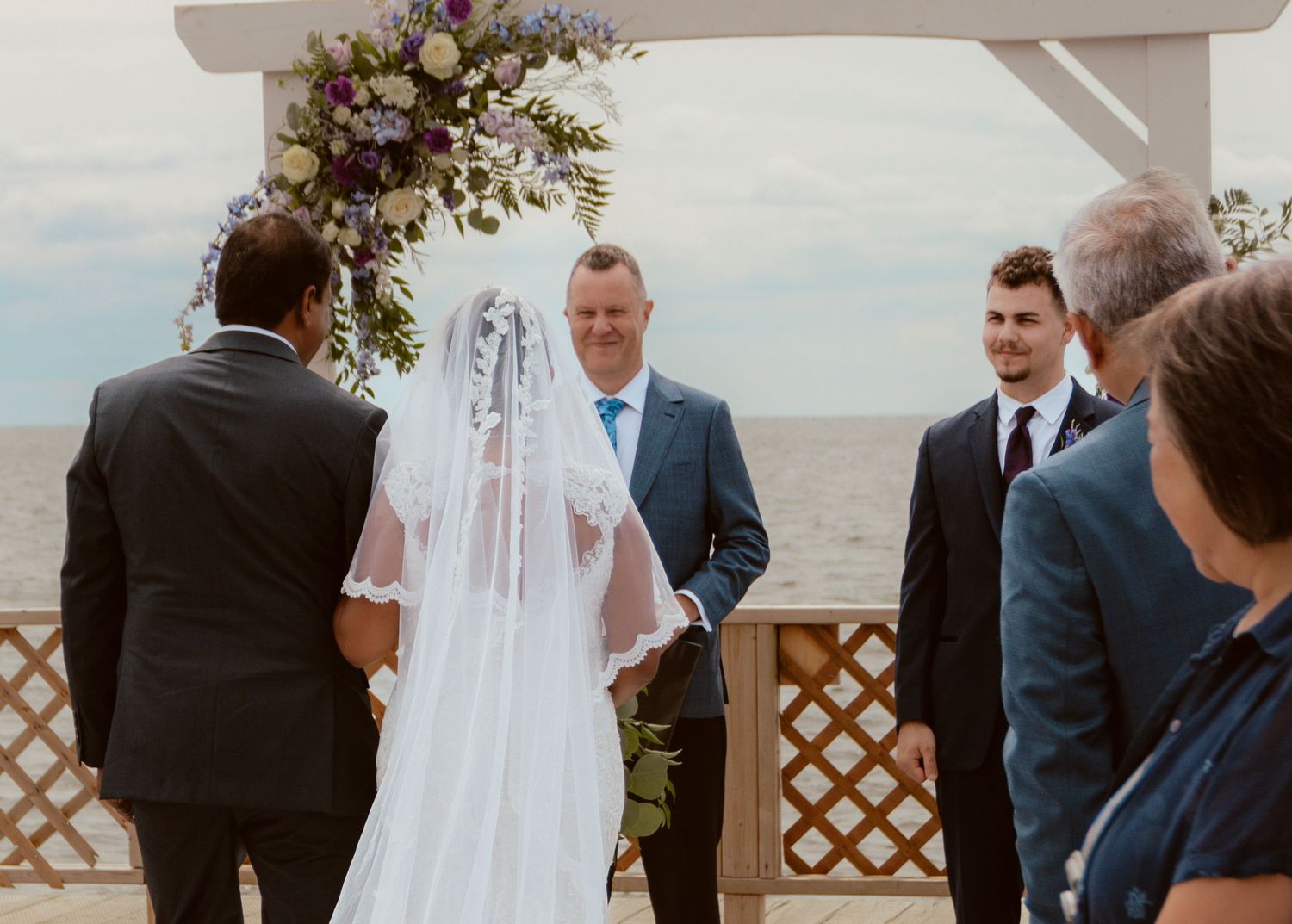 An outdoor wedding ceremony under a floral arch with ocean views.