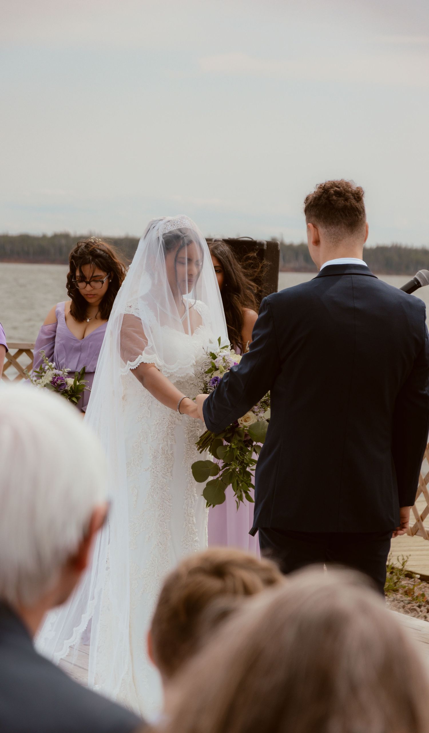 Lakeside wedding ceremony with couple exchanging vows in front of guests on a misty afternoon.