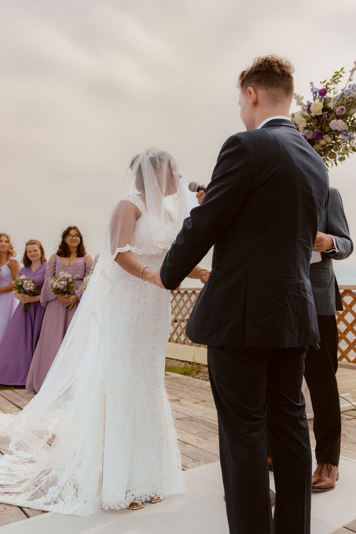 A wedding ceremony taking place outdoors with bridesmaids in purple dresses watching the couple at the altar.