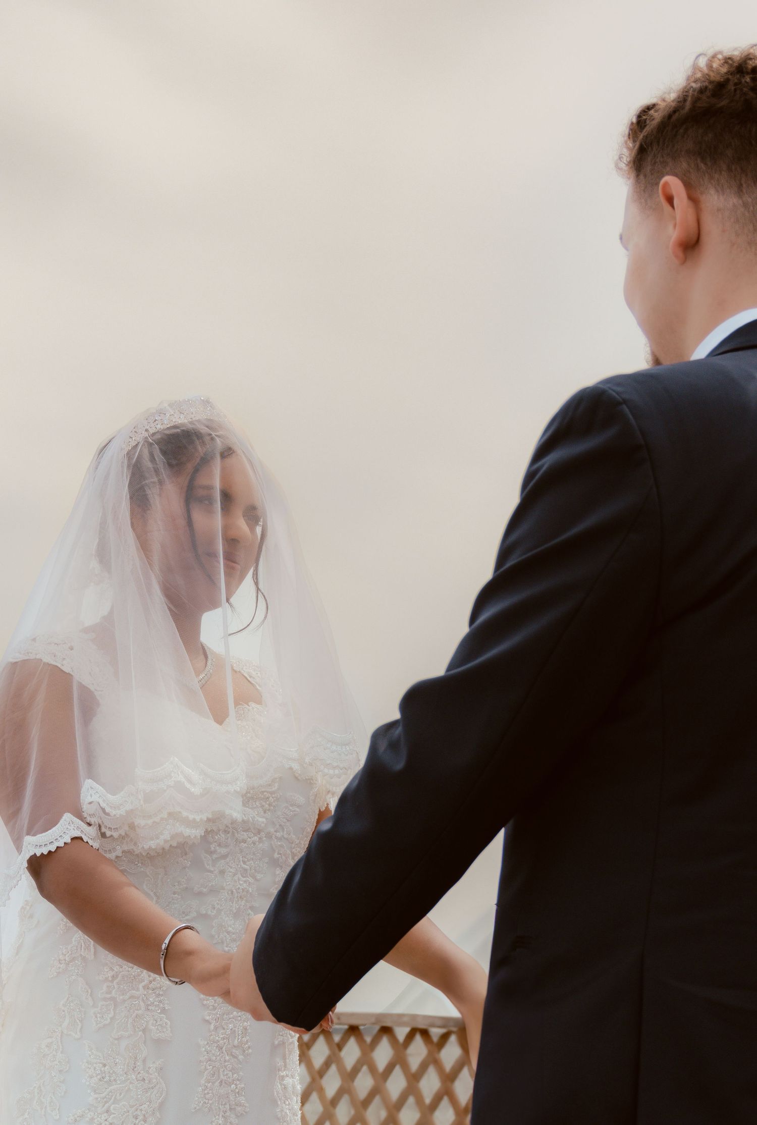 A close-up wedding moment with a bride in a white lace gown with veil and groom in a dark suit.