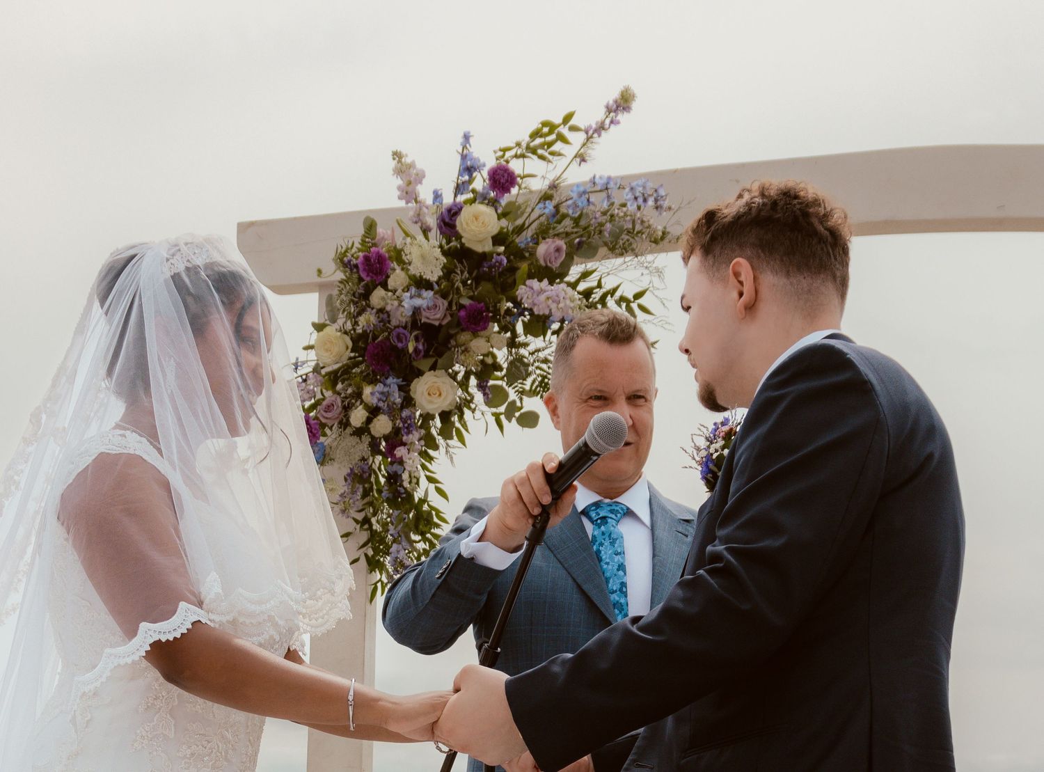 A happy wedding ceremony with the officiant and couple exchanging vows under a beautiful floral arrangement.