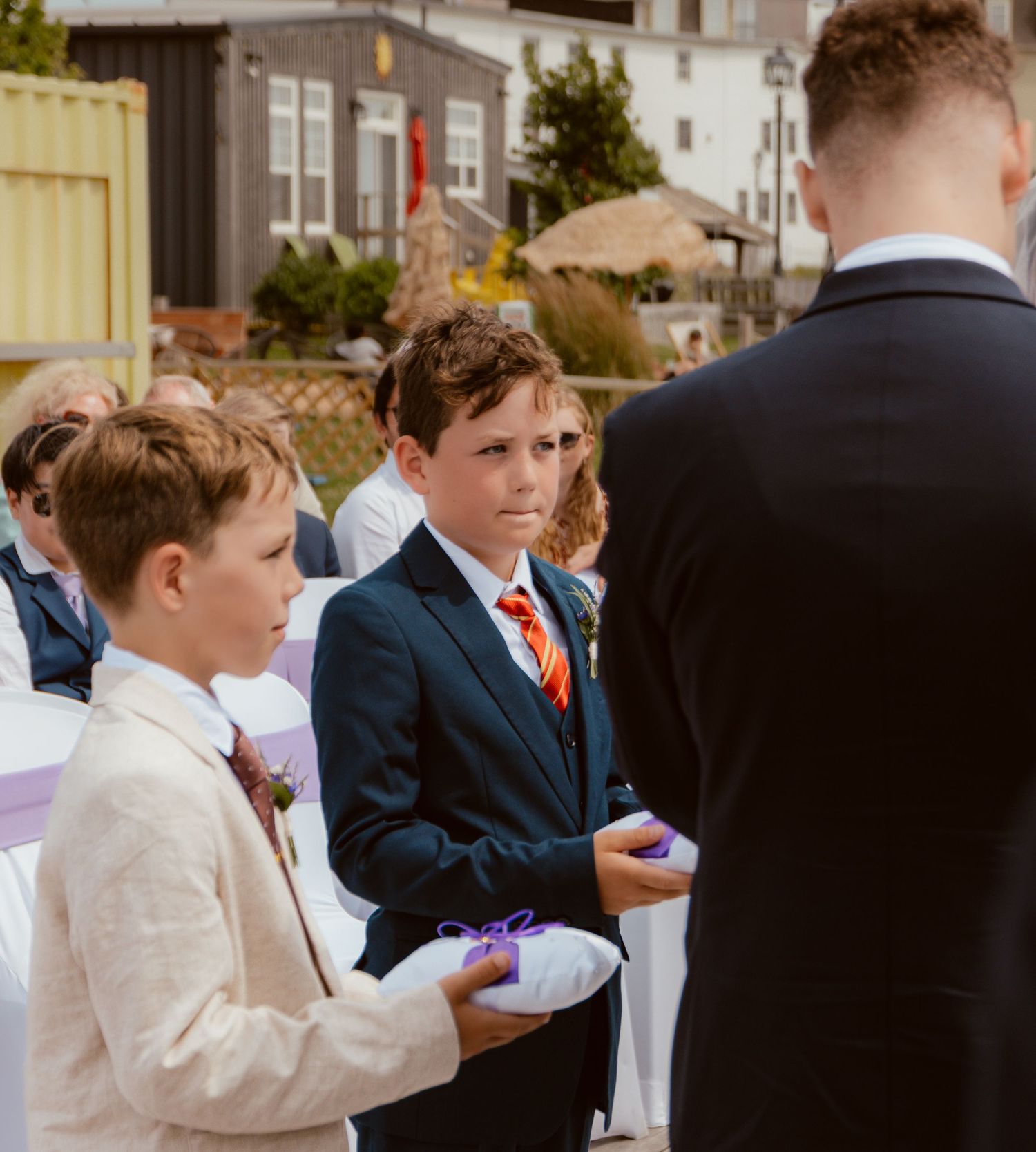 A group in formal attire during a wedding ceremony, with the individuals holding small purple items.