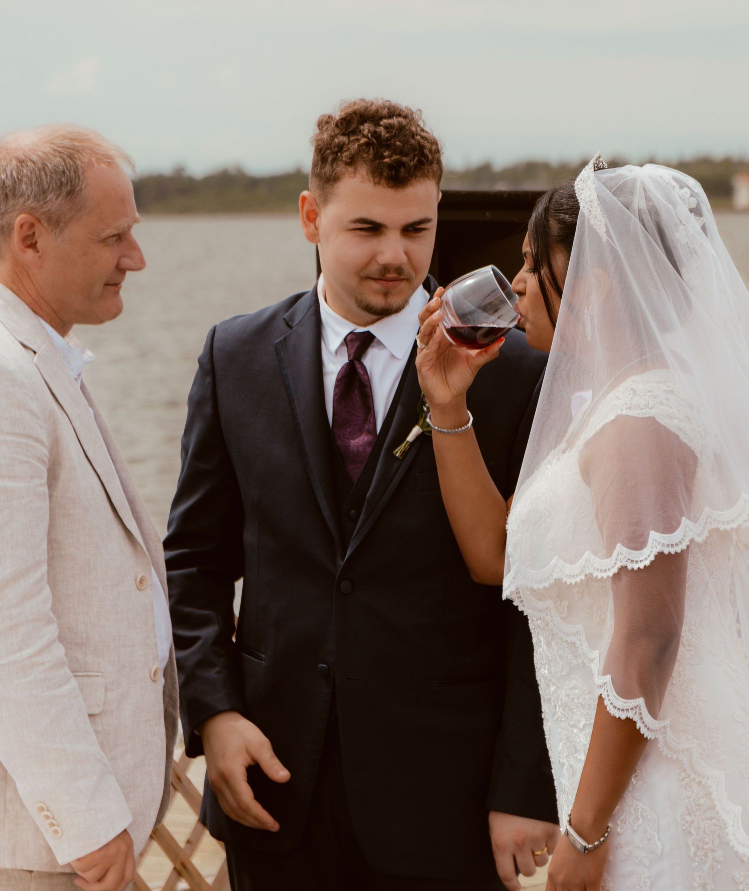 Bride takes a sip of wine during an outdoor waterfront wedding ceremony.