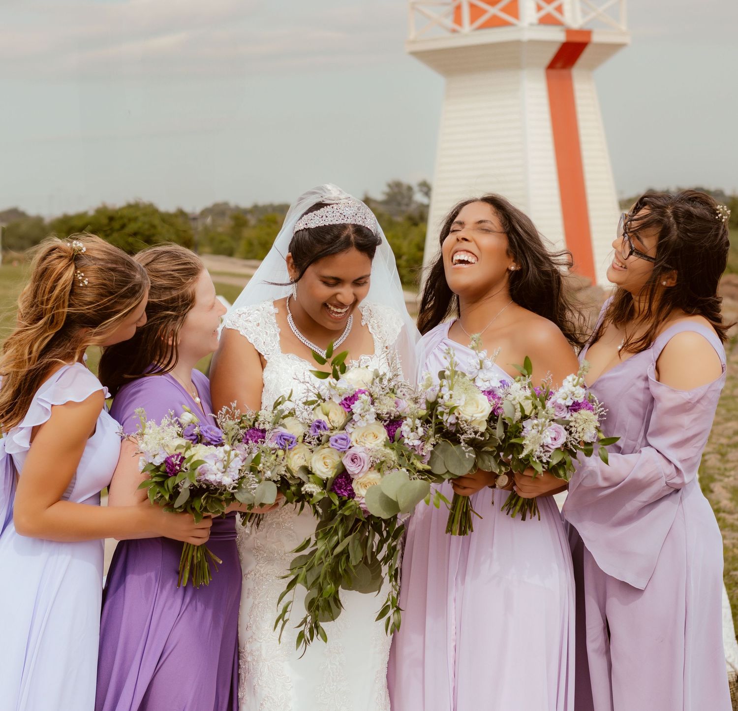 Bridal party in purple dresses laughs together while holding floral bouquets.