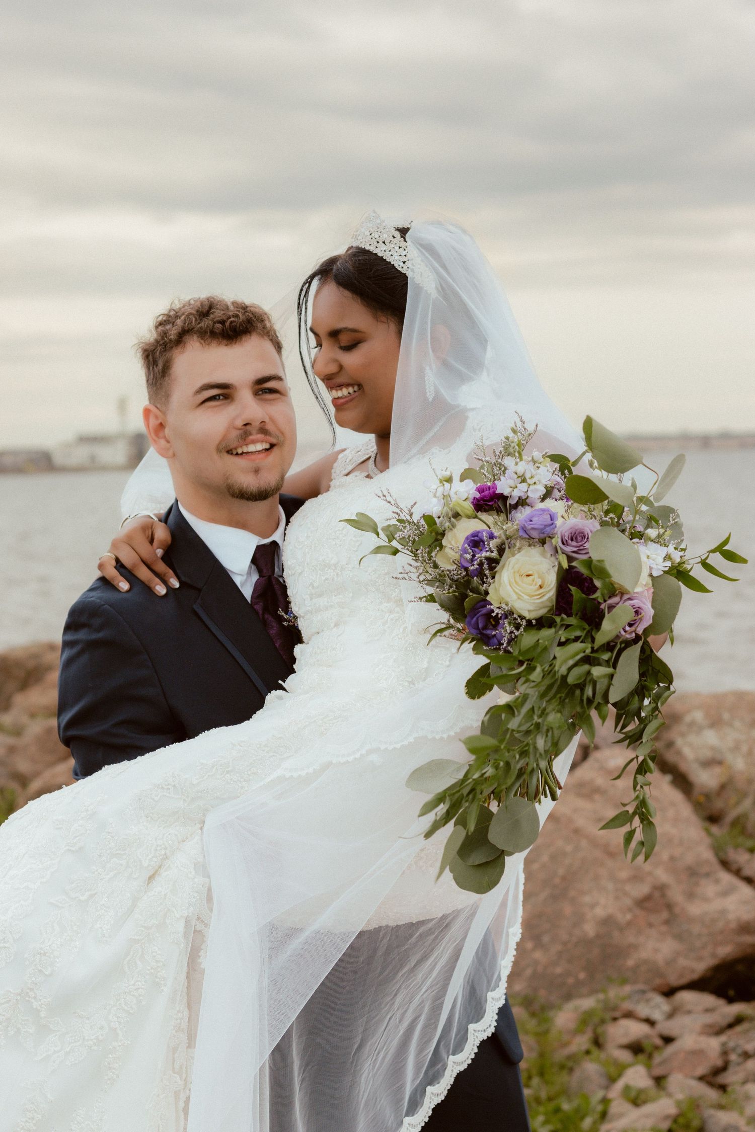 Couple shares romantic moment on rocky shore during coastal wedding photoshoot.