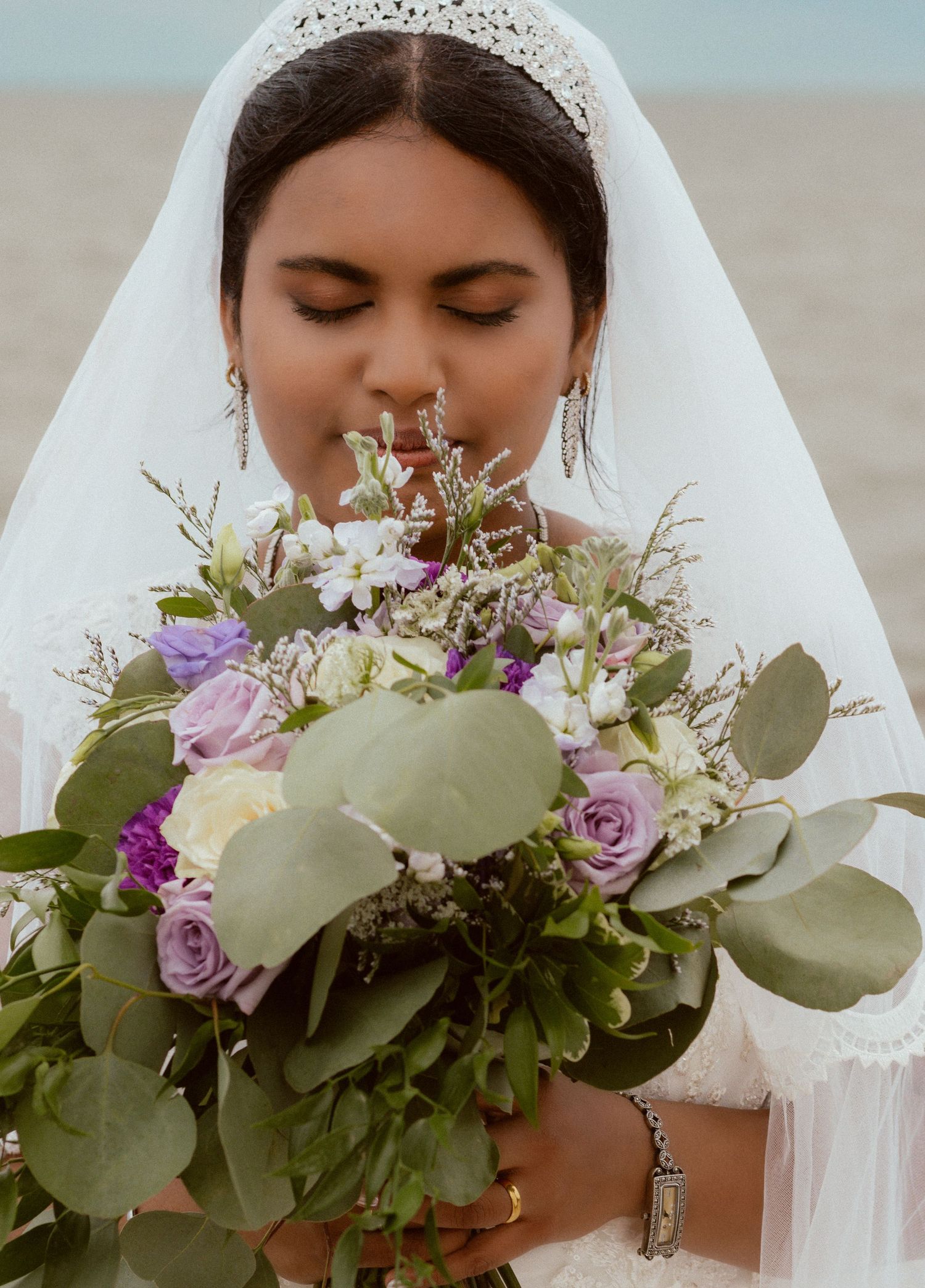 Close-up of bridal bouquet featuring lavender roses and eucalyptus leaves with flowing white veil.