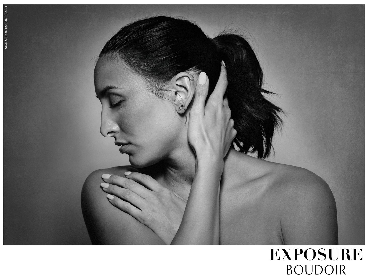 Artistic black and white boudoir photography showing subject in profile with hand on neck in dramatic lighting.